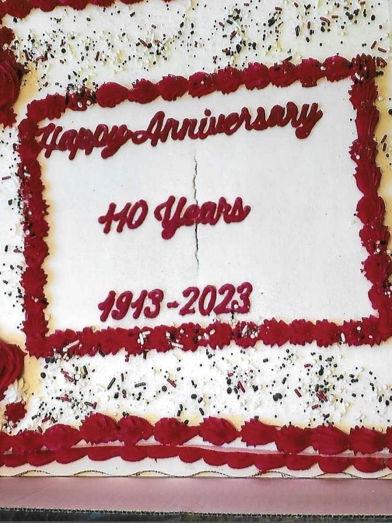A celebratory cake decorated with red icing, featuring the words 'Happy Anniversary,' '110 Years,' and '1913-2023.'