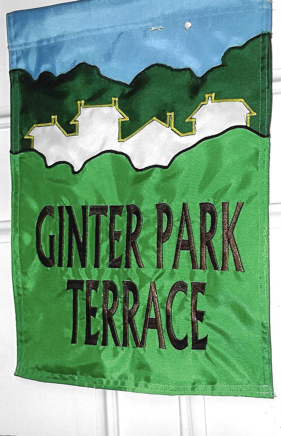 Garden flag displaying 'GINTER PARK TERRACE' in bold letters, with an artistic depiction of houses and green hills under a blue sky.